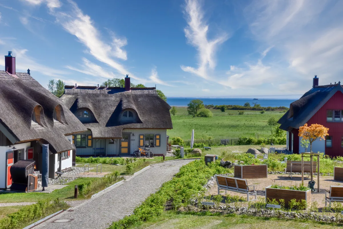 Reetgedeckte Ferienhäuser im Feriendorf Klein Stresow mit Blick über die Wiesen zum Wasser